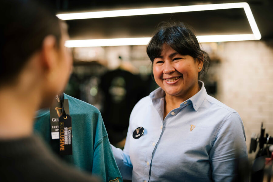 A smiling woman who works in the Guinness Storehouse serving a customer in the retail store.