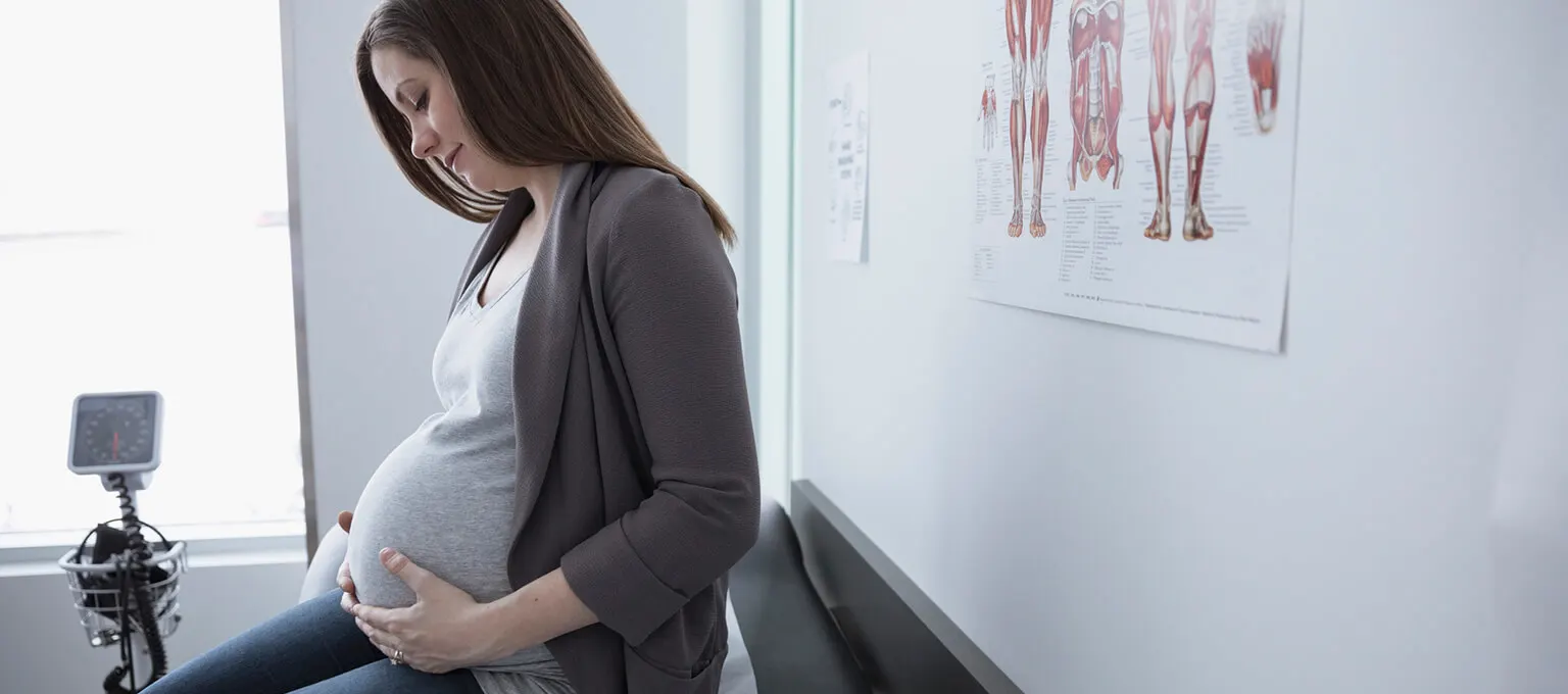 Epidural: A pregnant woman contemplates her belly on the table in the doctor’s office