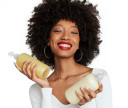 Happy woman with healthy, coily hair holds her customized shampoo and customized conditioner in sunkissed yellow formula. 