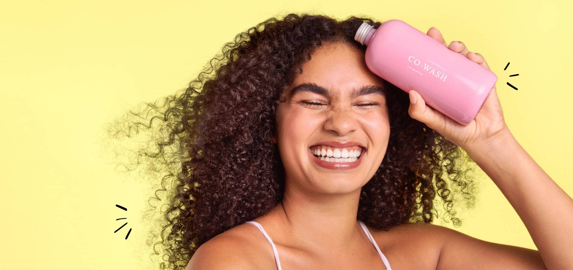 Model with brown curly hair and pink co wash bottle