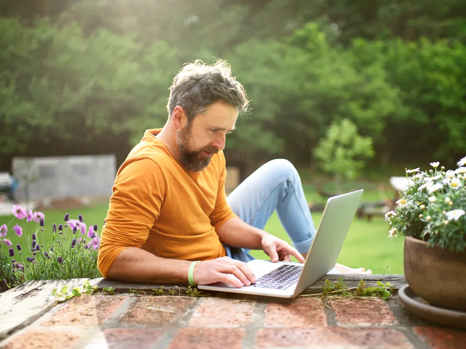 Digital Wissen, Mann im gelben Pull sitzt im Garten am Laptop