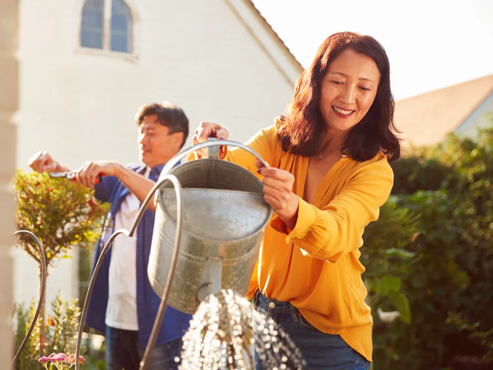 Paar im mittleren Alter bewässert Pflanzen im Garten an einem sonnigen Tag
