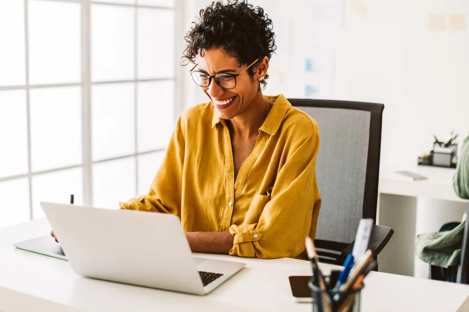 Transformation meistern - Frau in gelber Bluse sitzt lächelnd am laptop