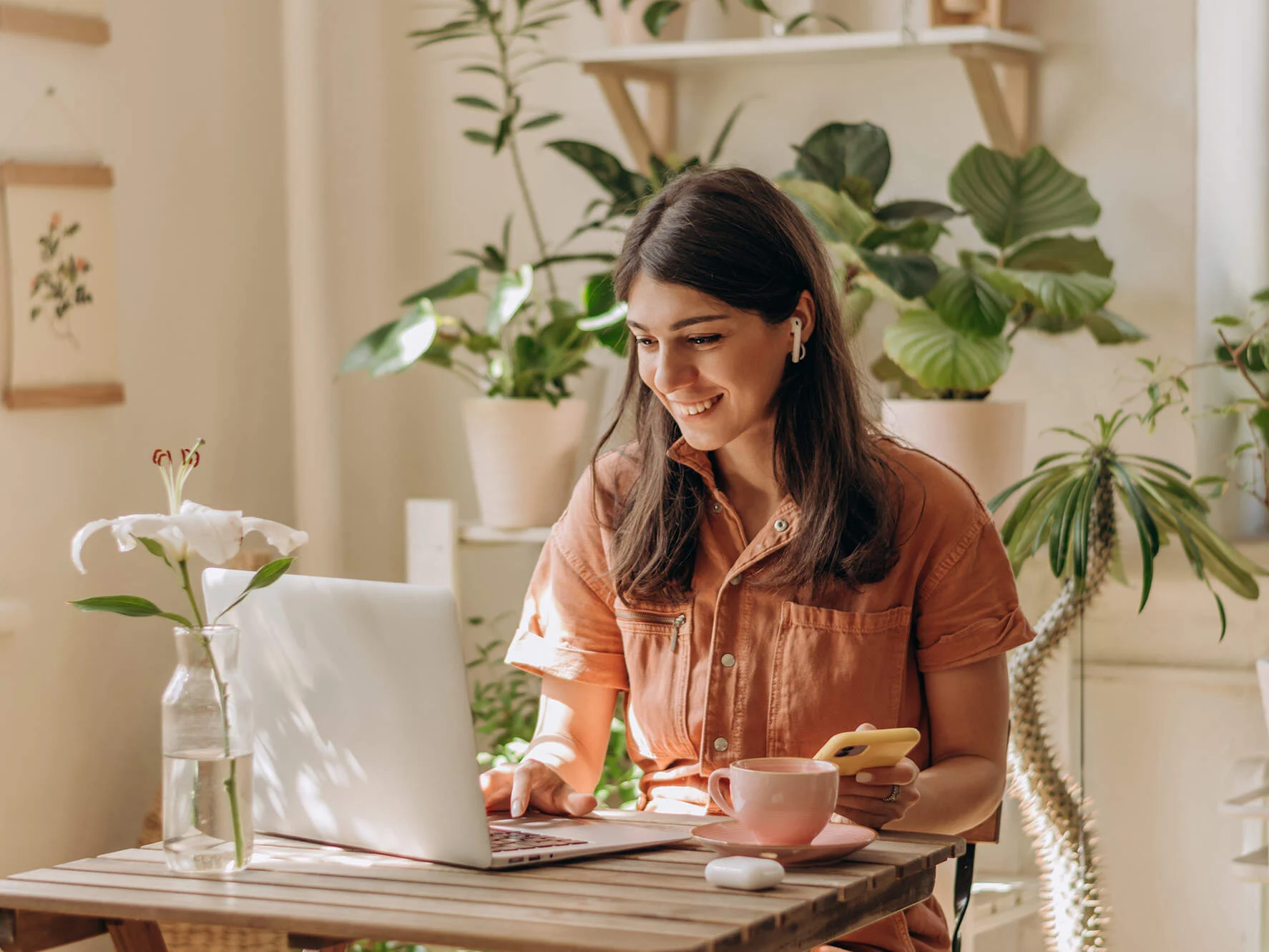 VPN einrichten - Frau sitzt im Büro am Laptop mit Handy und ein Kaffee steht