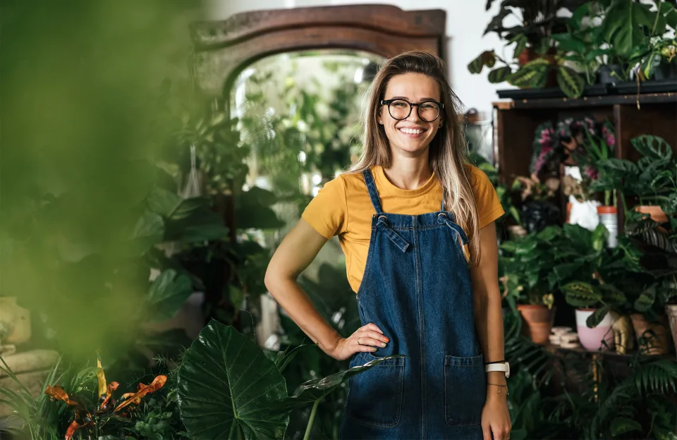 Zukunftssichere Technologie - Frau in Jeans Overall lächelt und steht in einem Pflanzengeschäft