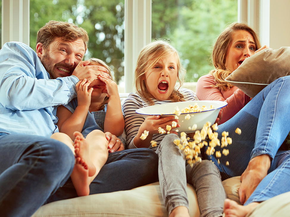 Familie sitzt auf dem Sofa und schauen einen spannenden Film, Popcorn fliegt aus der Schüssel