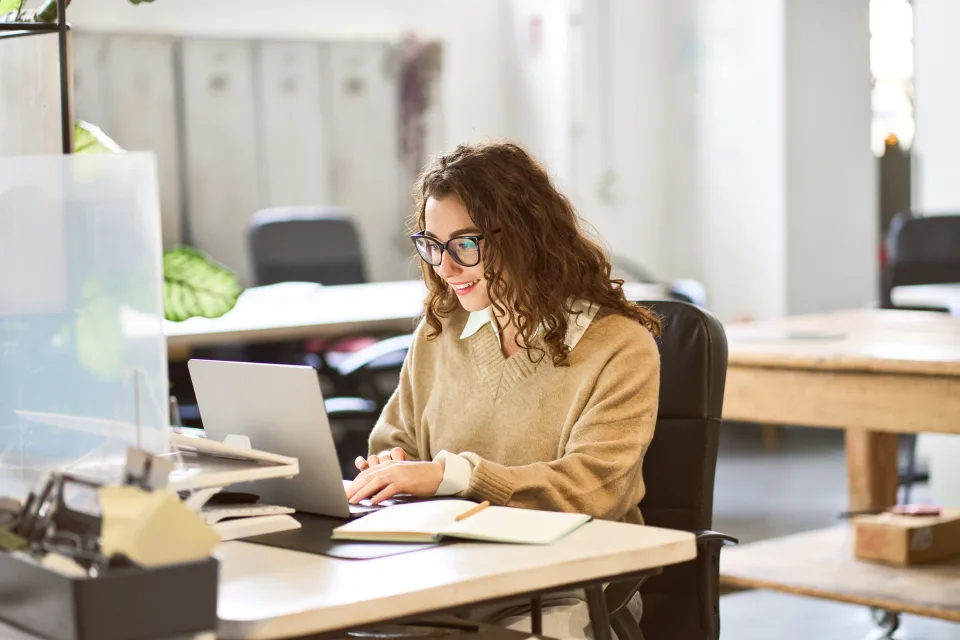  Organisatorische Herausforderung - Frau sitzt am Arbeitsplatz am Laptop