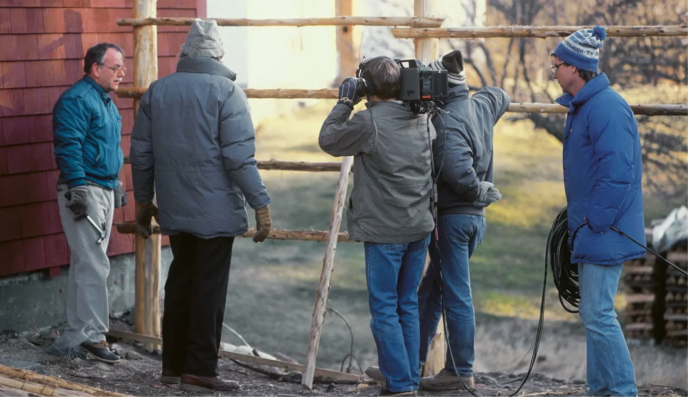 camera crew on location filming a man next to a wooden fence