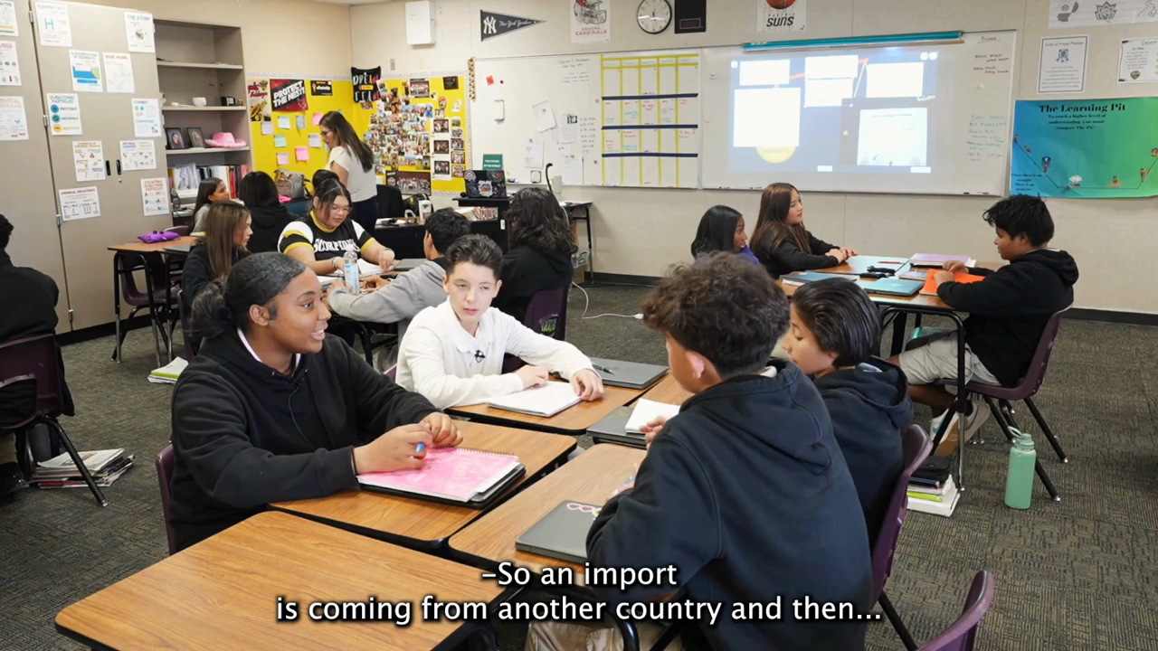 High school students sitting around tables in a classroom collaboratively discussing concepts of imports and exports to deepen their understanding.