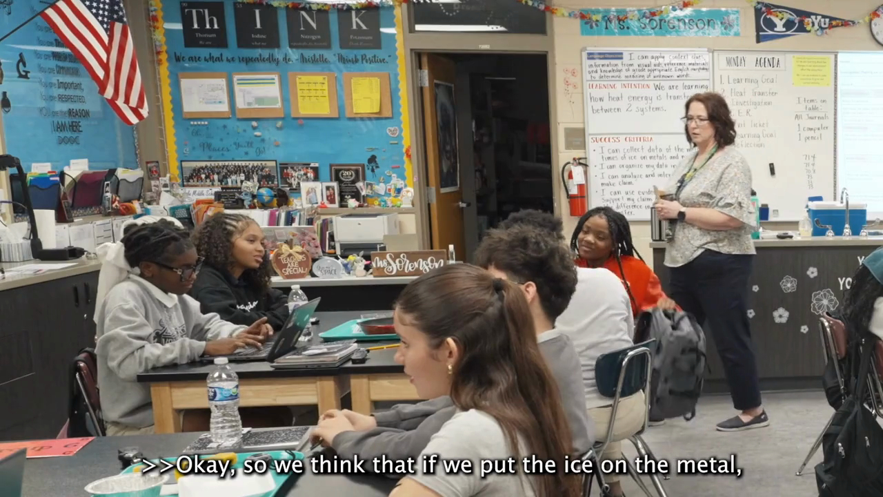 Video thumbnail of a middle school science classroom where students sit at lab tables with laptops while their teacher stands near a whiteboard showing a learning intention about heat transfer. 