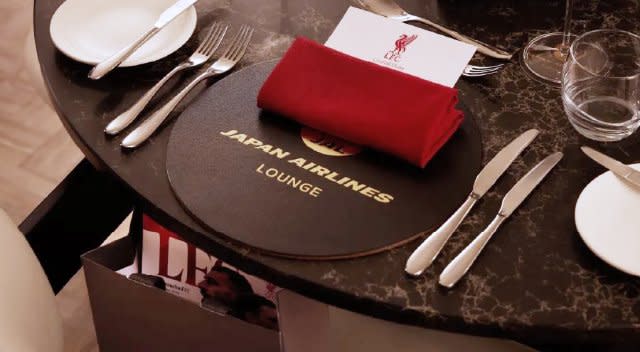 Table dressée avec un set de table Japan Airlines Lounge, une serviette rouge, des couverts, des verres et une carte de menu LFC.