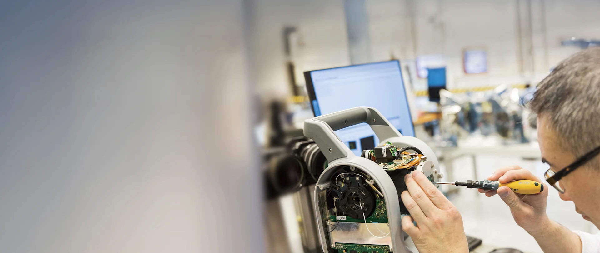 A repair technician in glasses works on a piece of Trimble equipment with a screwdriver.
