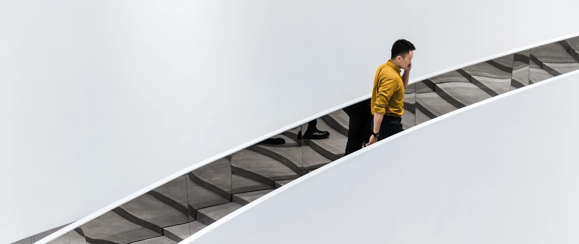 Eine Person in einem gelben Hemd mit hochgekrempelten Ärmeln telefoniert und geht dabei eine Treppe hinauf.