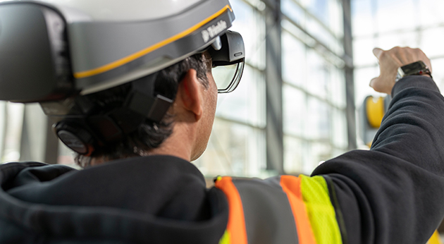 A professional wearing a Trimble XR10 with HoloLens 2 mixed reality hard hat points toward a construction site.