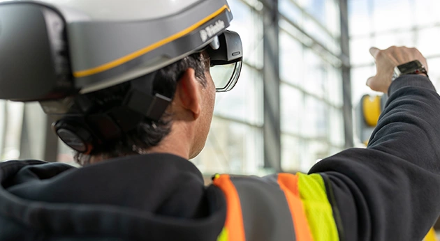 A professional wearing a Trimble XR10 with HoloLens 2 mixed reality hard hat points toward a construction site.