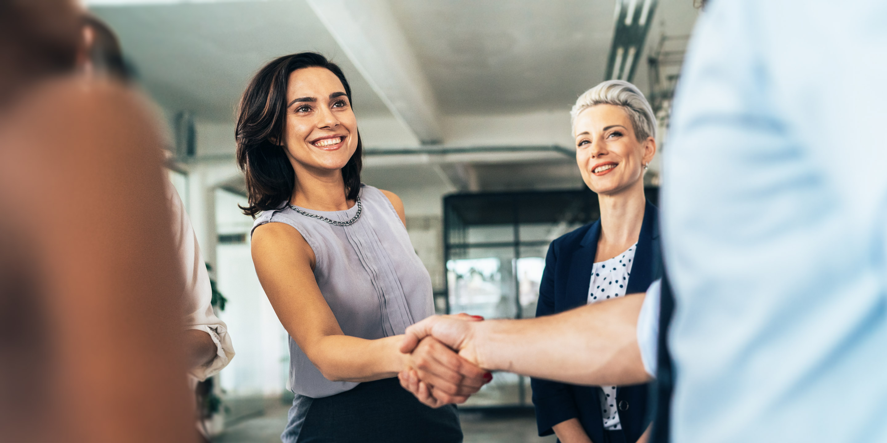 Two professional women shaking hands and smiling at an indoor business meeting