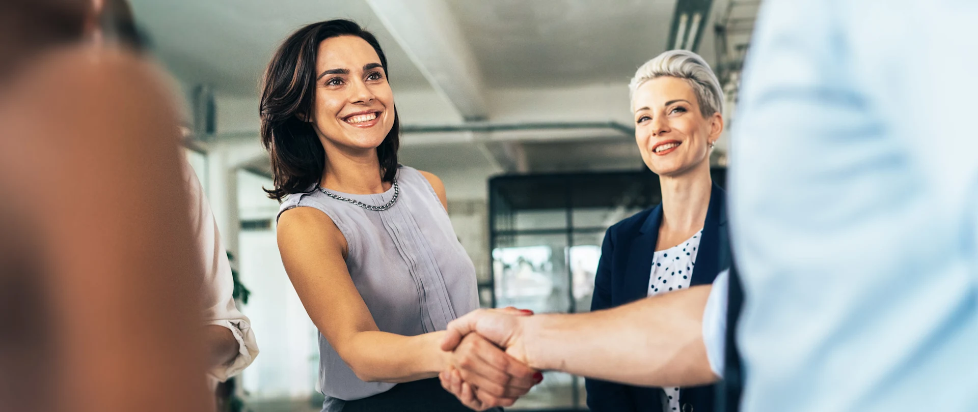 Twee professionele vrouwen schudden elkaar de hand en glimlachen tijdens een zakelijke bijeenkomst binnen