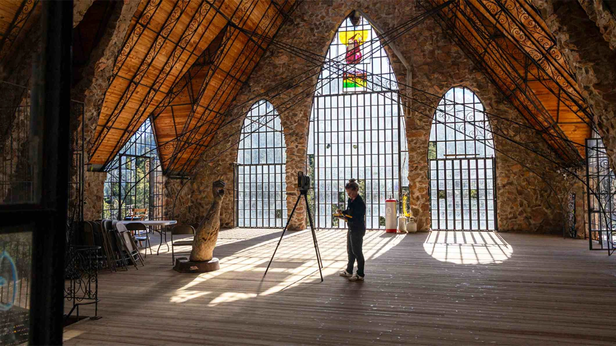 Eine Person vermisst das Innere von Bishop Castle, CO, mit einem Trimble-X9-Laserscanner und einem T10X-Tablet. Es sind Bogenfenster und eine Handskulptur zu sehen.