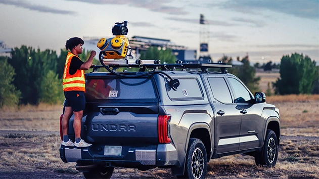 Man met reflecterend vest aan de achterkant van een auto die de mobiele mappingtechnologie van Trimble opzet