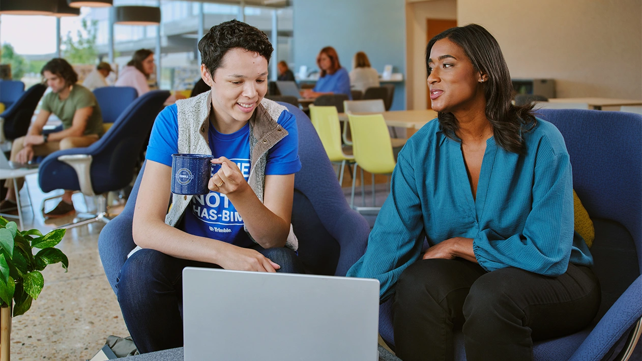 Two young professionals talking in casual setting while using laptop