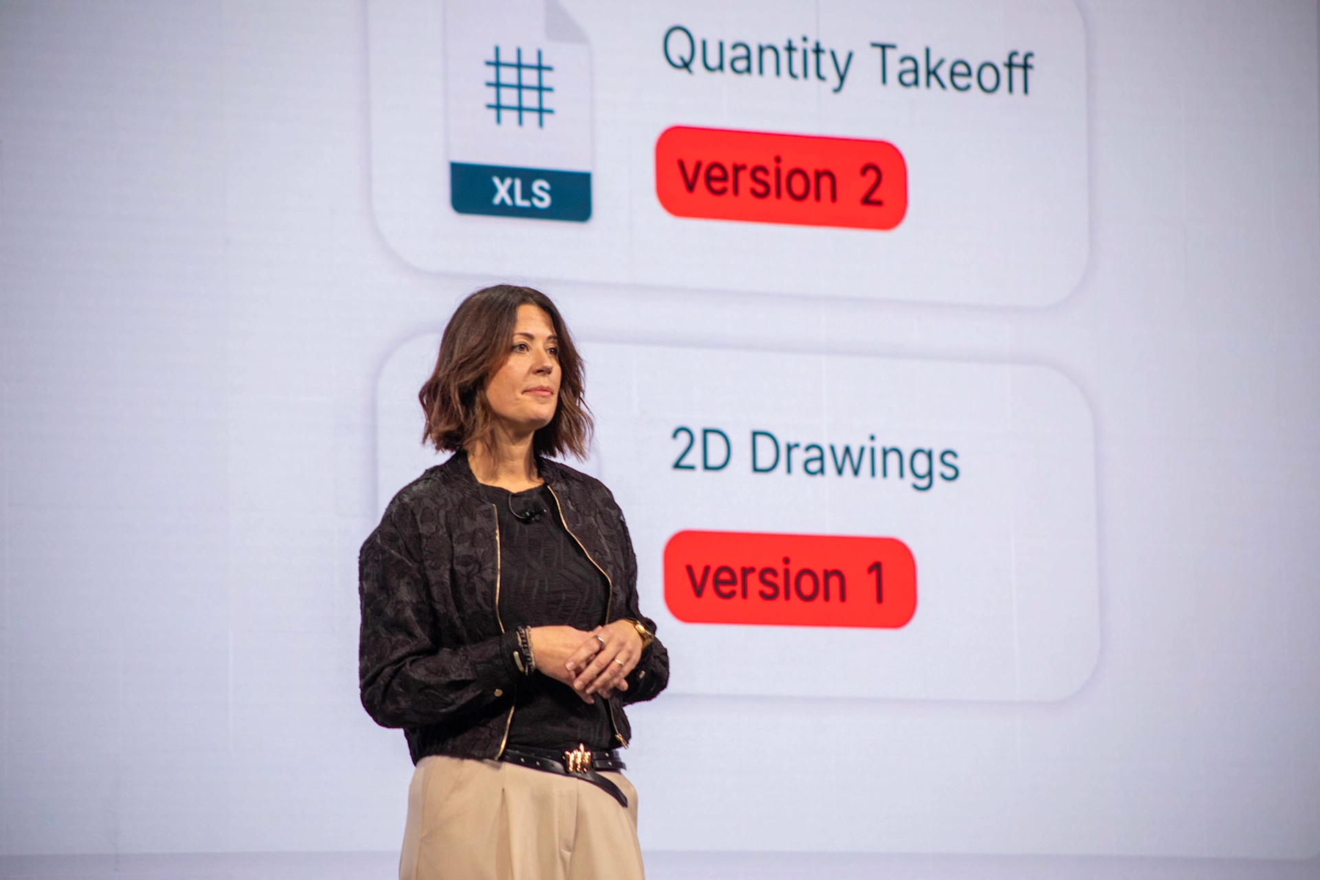 A woman presents Trimble software updates for Quantity Takeoff (version 2) and 2D Drawings (version 1) on a large screen at a conference.