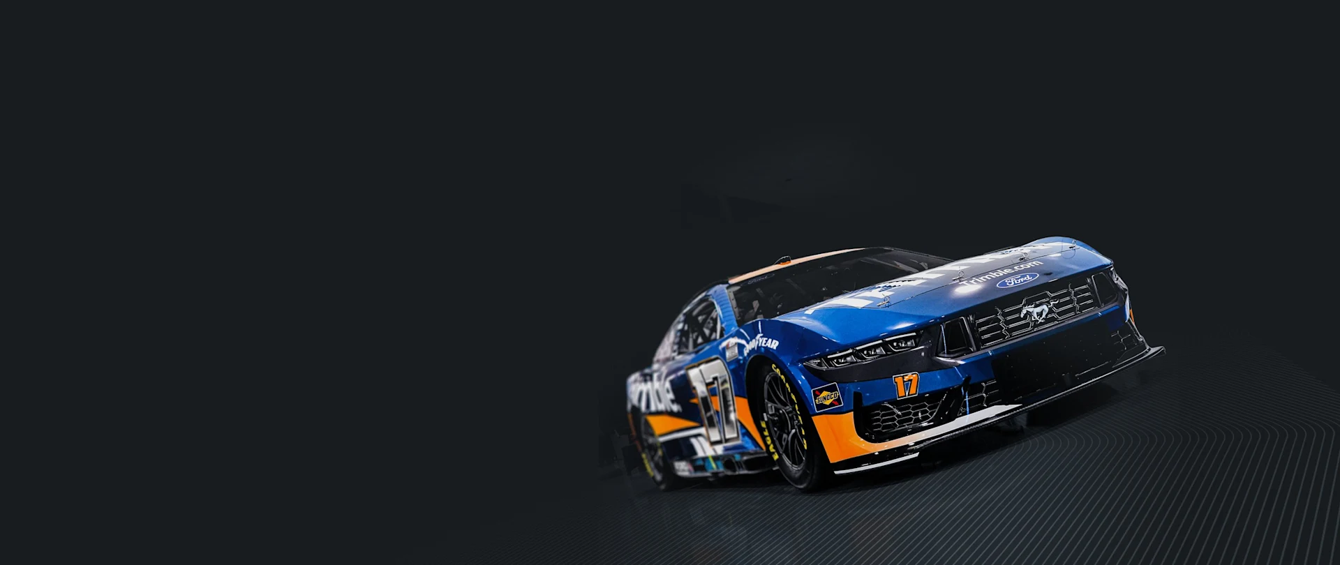 A blue and orange No. 17 Trimble Ford Mustang race car driven by Chris Buescher for RFK Racing, set against a dark, minimalist background.