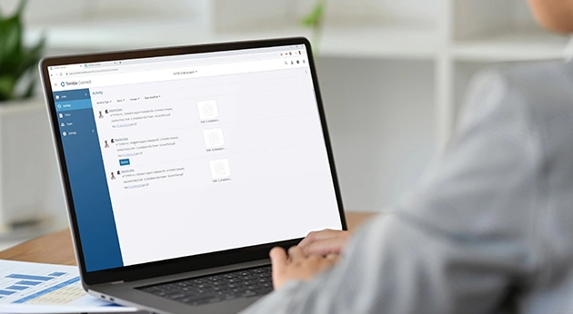 A woman uses Trimble Connect on a laptop to manage project activity and construction data in an office environment.