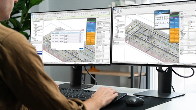 A person using Stabicad for Revit on dual monitors to design complex 3D MEP building systems, including electrical and ventilation routing.