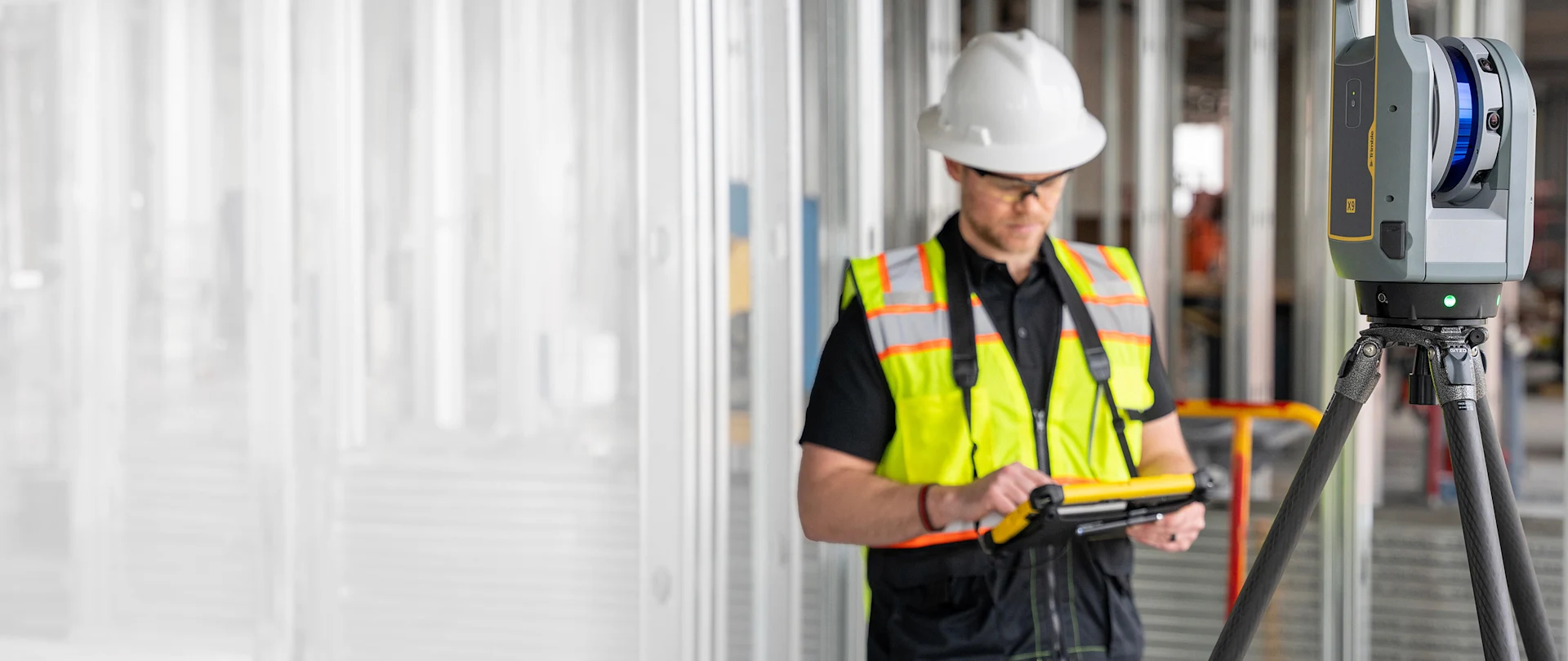 Construction worker using a Trimble tablet to operate a Trimble X9 3D laser scanner on a Gitzo tripod at a job site.