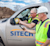 Two construction workers in vests and hard hats look at a device mounted to a SITECH truck window.