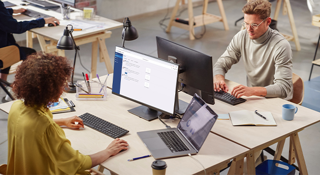 Office workers using computers. A monitor displays the Trimble Connect dashboard while a laptop shows data visualizations.