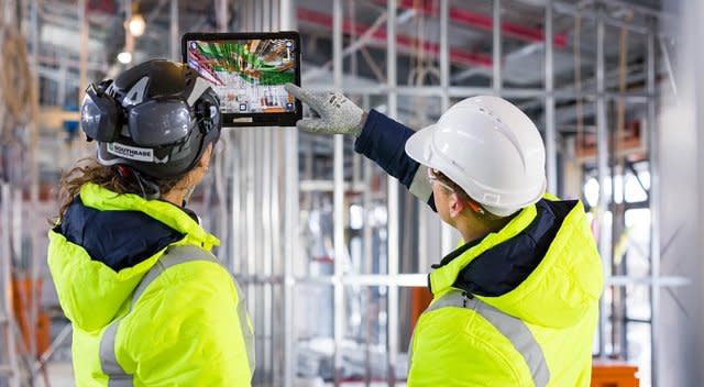Zwei Bauprofis auf einer Baustelle betrachten ein robustes Tablet mit AR-BIM-Überlagerung von Bausystemen.