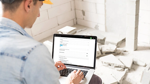 A construction worker uses the Trimble Viewpoint portal on a laptop at a job site.