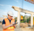 An engineer in a white hard hat and orange safety vest uses a tablet and stylus at a bridge construction site with concrete supports.