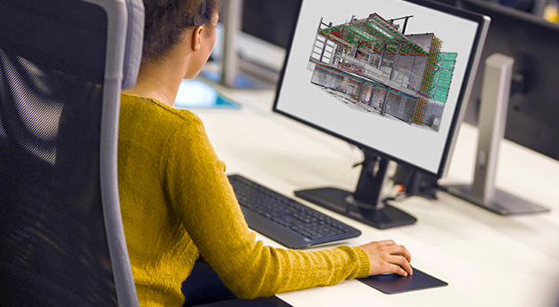 A woman uses Trimble’s 3D modeling software to review a detailed structural building model on a computer screen.