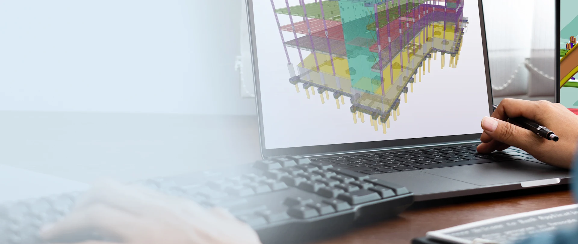 A person uses Trimble’s Tekla Structures software on a laptop to design a colorful 3D structural model of a multi-story building.