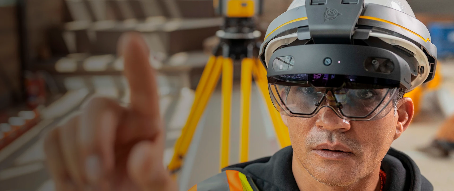 Man looking at camera pointing while using Trimble HoloLens with scanning equipment in background