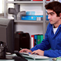 A person in a blue jumpsuit sits at a desk and types on a computer keyboard