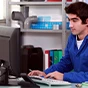 Iemand in een blauwe overall zit aan een bureau en typt op een computertoetsenbord