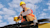 Construction engineer with hard hat and protective vest on top of heavy machinery using Trimble Geospatial equipment