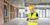 A person wearing a hard hat and safety vest on a jobsite using mobile construction procurement software