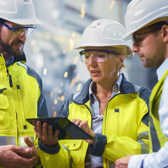 Three communications professionals with hardhats looking at tablet device