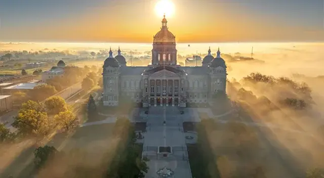 Aerial view of the Iowa State Capitol, a Renaissance Revival edifice with its central 23.75-karat gold leaf dome and four smaller copper domes, emerging from sunrise fog.