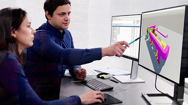Two engineers collaborate at a desk, with one pointing a pen toward a 3D MEP design within Trimble Nova software on a computer monitor.