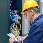 Man in yellow hard hat using tablet near data server room