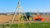 A Trimble Spectra Precision GL700 laser transmitter on a tripod guides a tractor leveling a field with an orange scraper in the background.