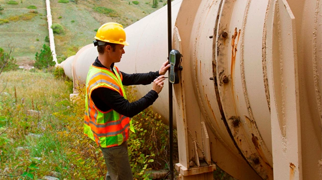 Engineer using Trimble geospatial technology next to oil and gas pipe