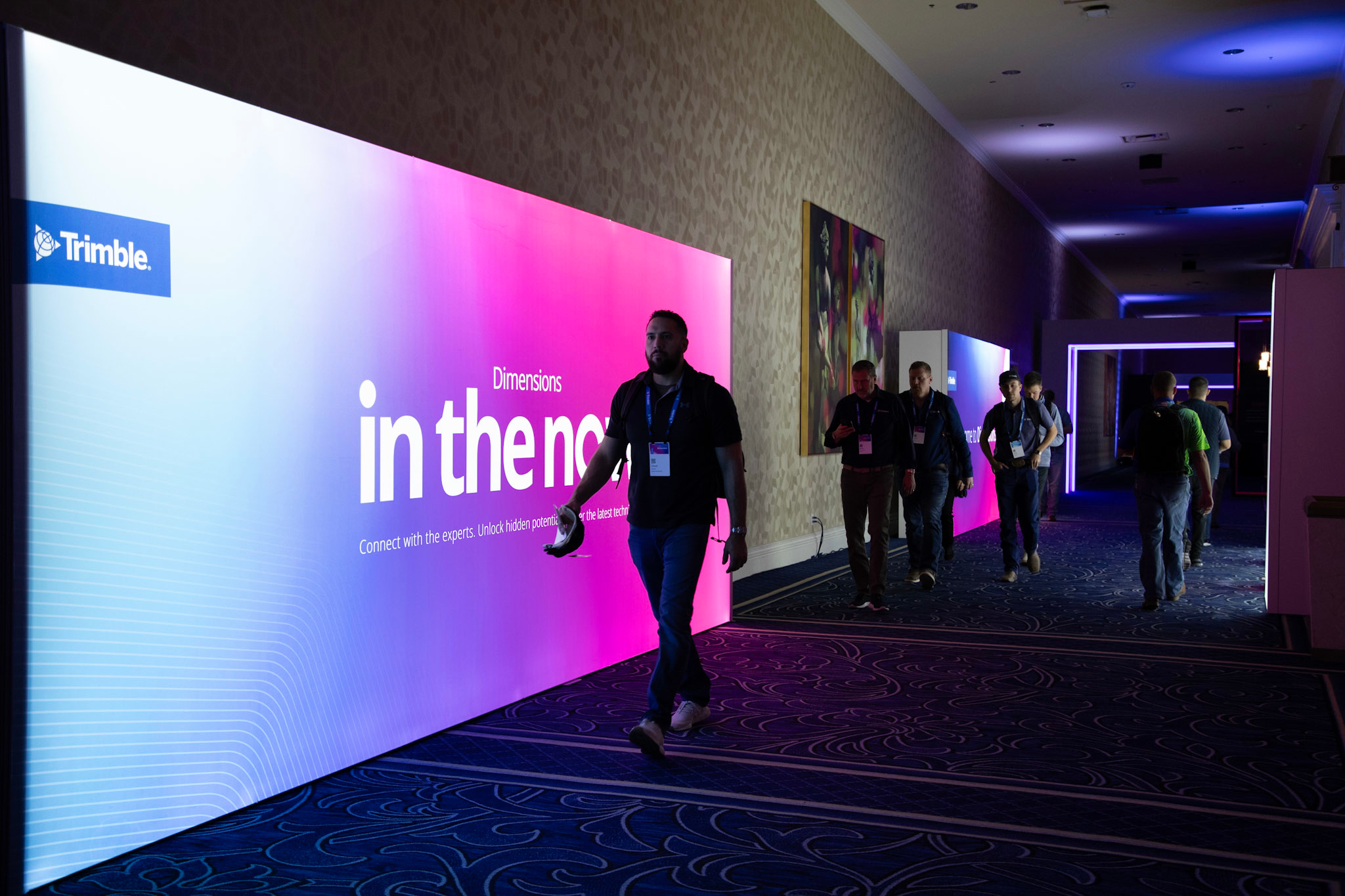 Attendees walk by glowing screens with Dimensions branding in the immersion tunnel as they exit the Expo Hall.