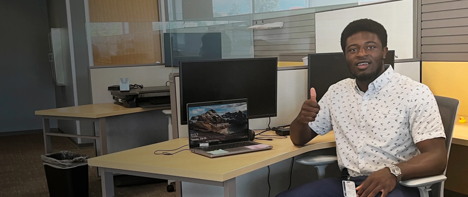 Young professional man at desk in front of computers smiling at camera giving a thumbs up