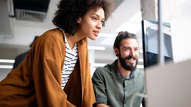 A man and a woman looking at a computer screen and smiling in a collaborative office setting.